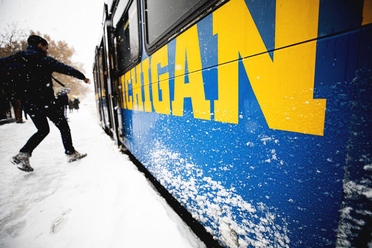 Student rushing to catch a snow covered University of Michigan blue bus in winter