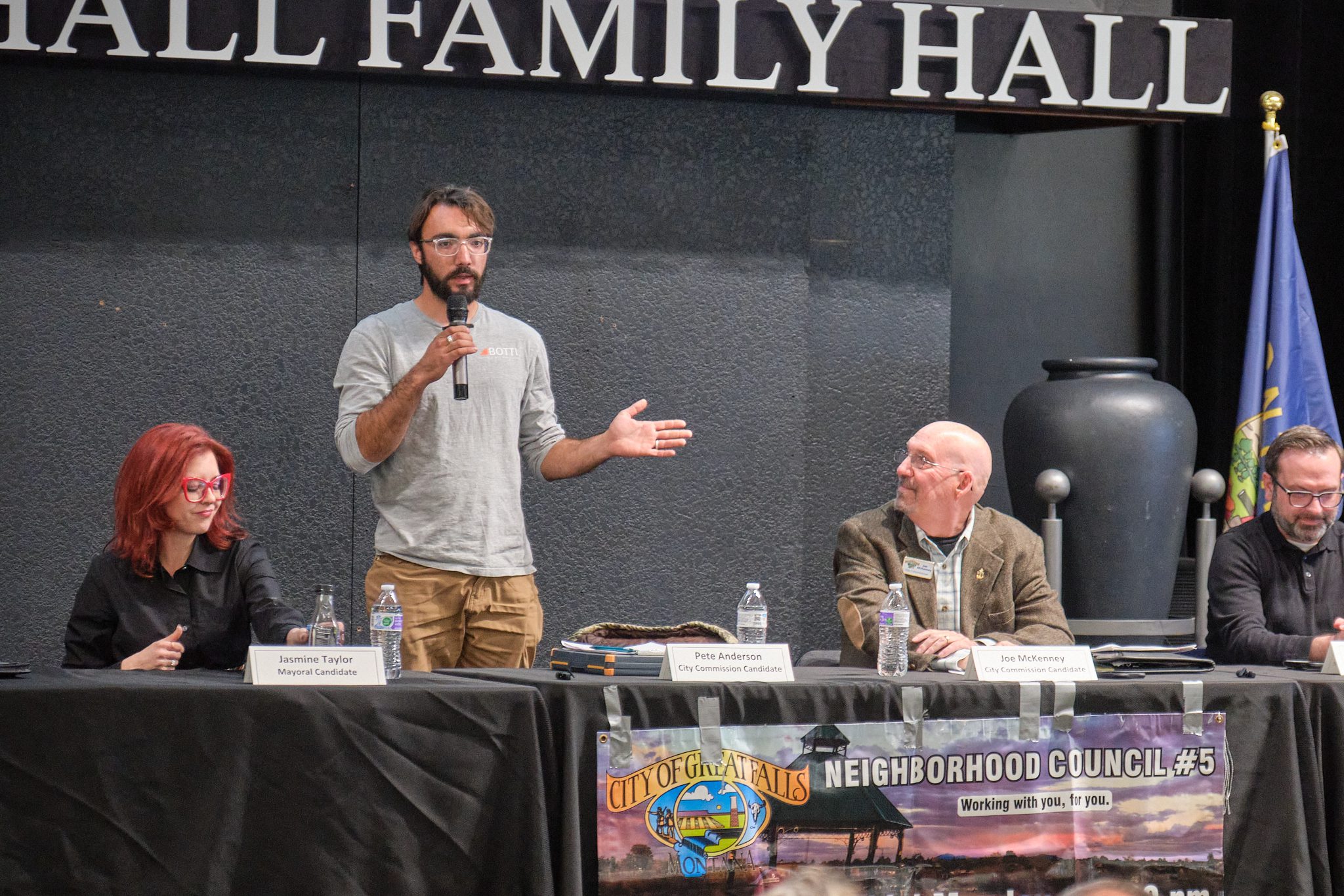 Pete Anderson speaks into a microphone at a candidate forum in Great Falls, seated with other local candidates under a 
