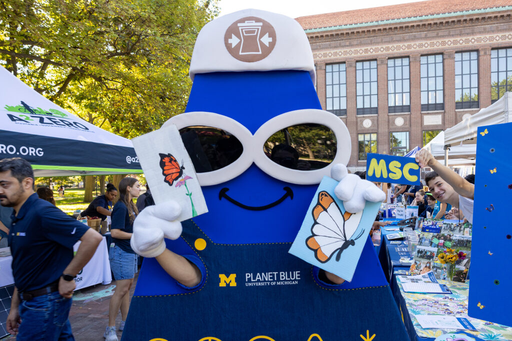 A blue mascot with large white glasses holding up two signs