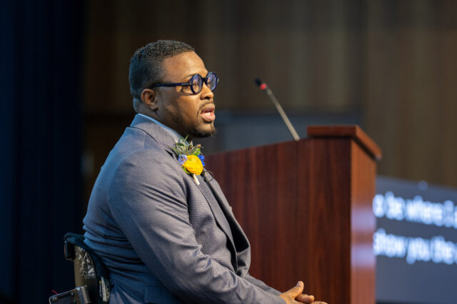 A man in a wheelchair speaks to a crowd at an award ceremony