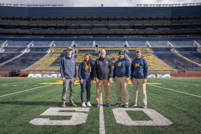 Five people standing on the 50-yard line in Michigan Stadium