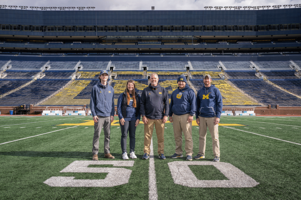 Five people standing on the 50-yard line in Michigan Stadium