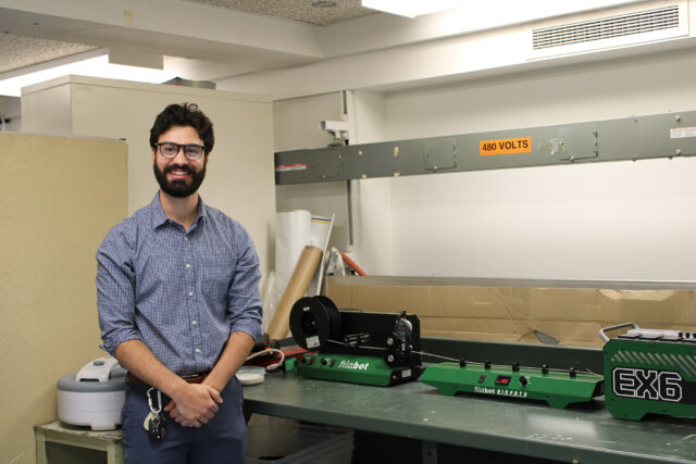 A man stands with his arms folded in front of him and smiles