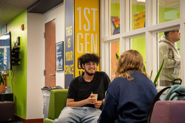 Two people face each other talking while seated in a room with lime green walls