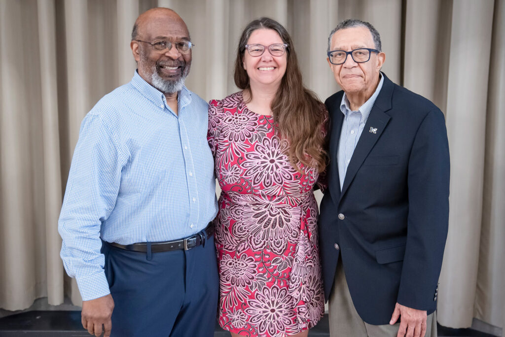 A woman surrounded by two men pose for a photograph