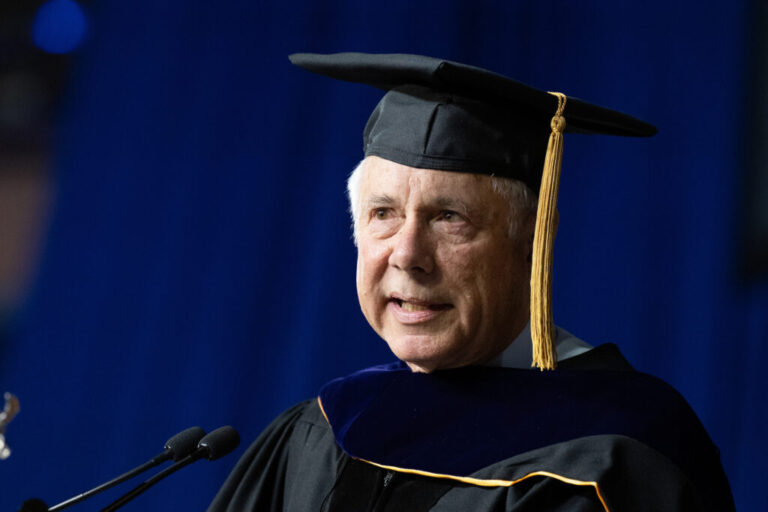 A man wearing a cap and gown speaks at a podium