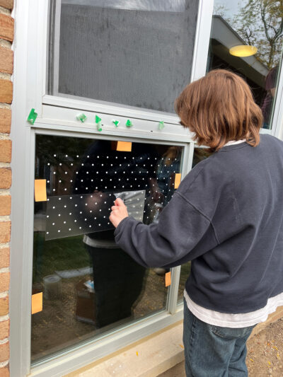 A person applies patterned film to a window of a building to help deter birds from striking it