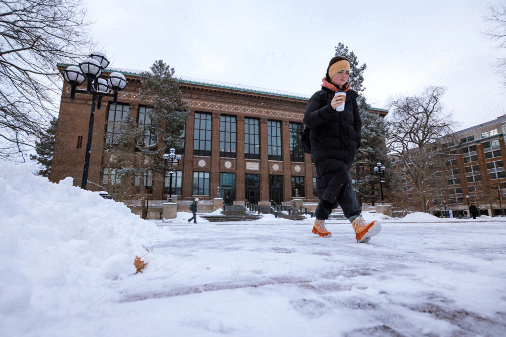 A student walks through the snow-covered Diag in front of Hatcher Gradute Library on a winter morning.