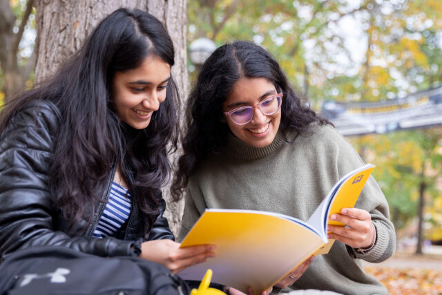 Two women smile as they read the same book
