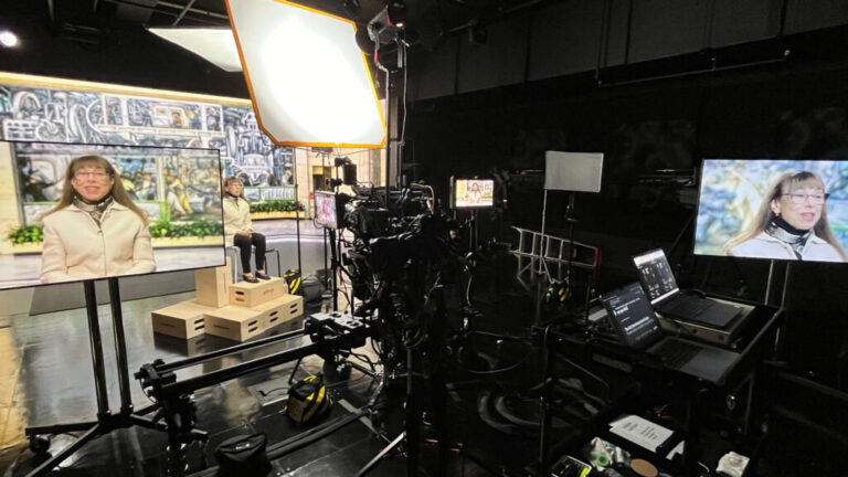 woman in a television studio with several monitors showing her face