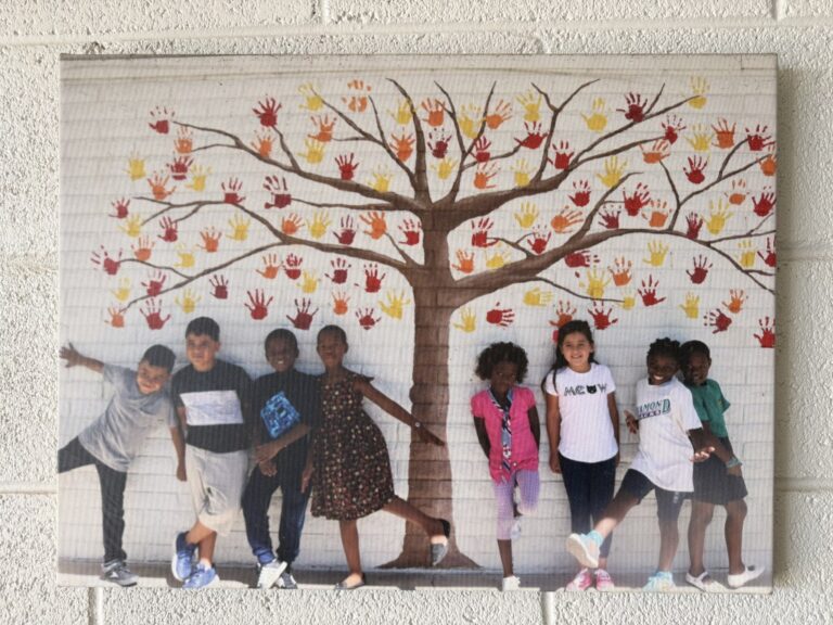 A photo of students standing under a tree with handprint leaves.