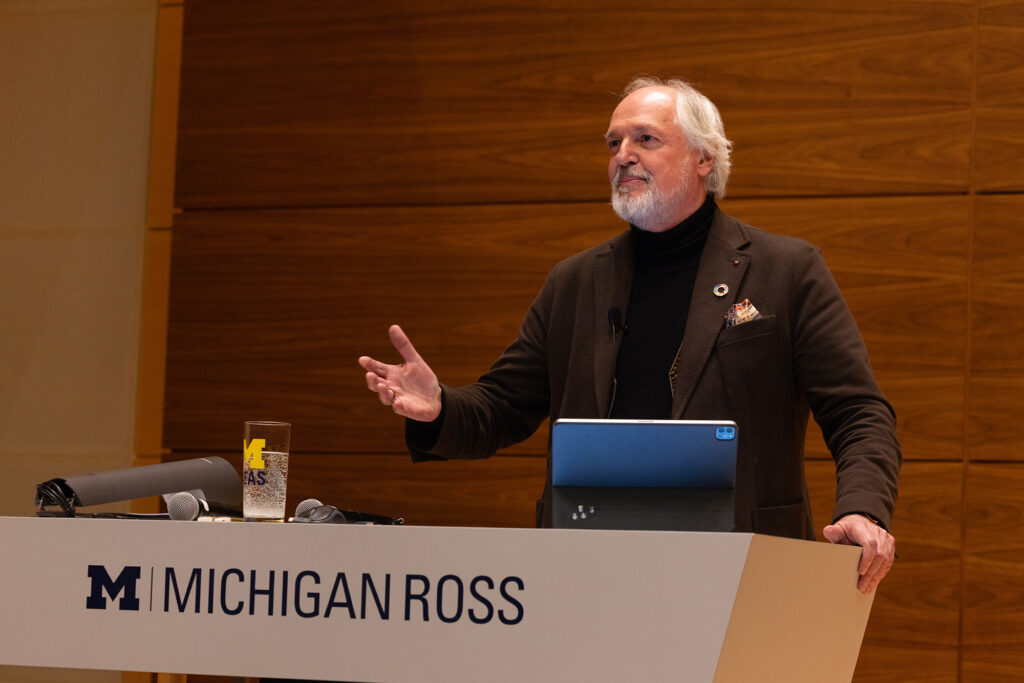 A man gestures with one hand while speaking behind a lectern that says Michigan Ross