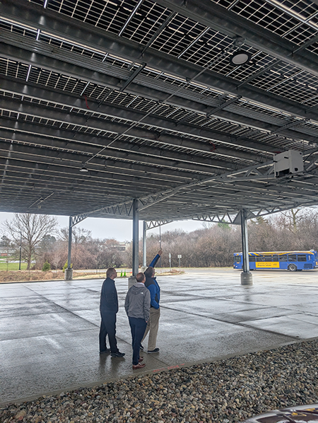 Three people stand underneath solar panels