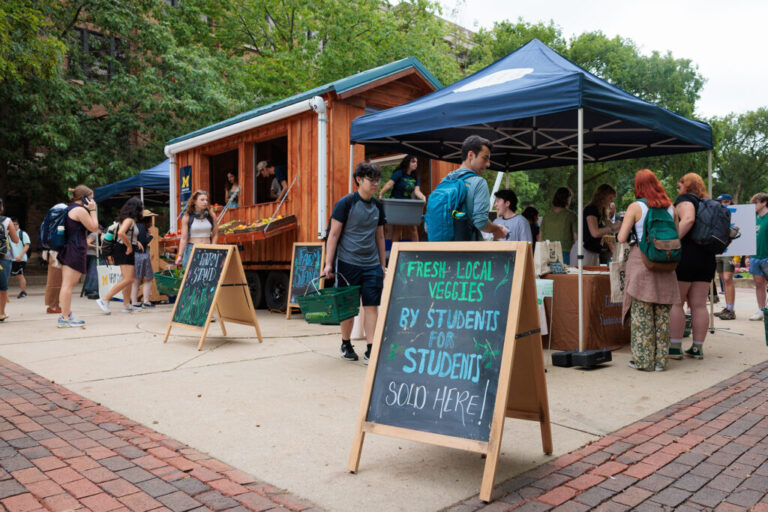 People shop for produce and other items at a small farm stand