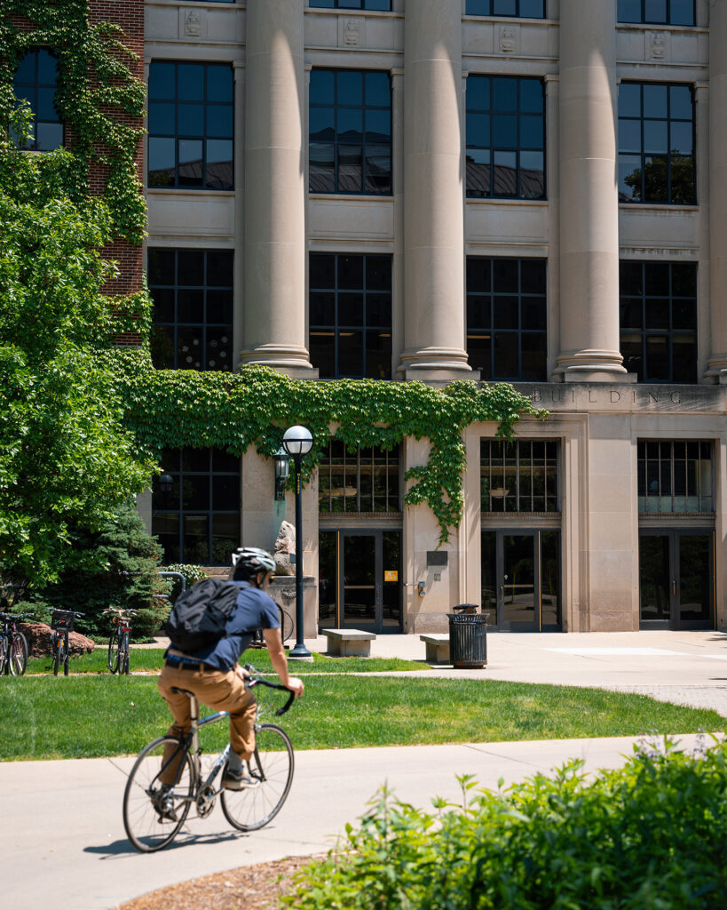 A cyclist passes the North University Building on a bright, sunny summer afternoon.