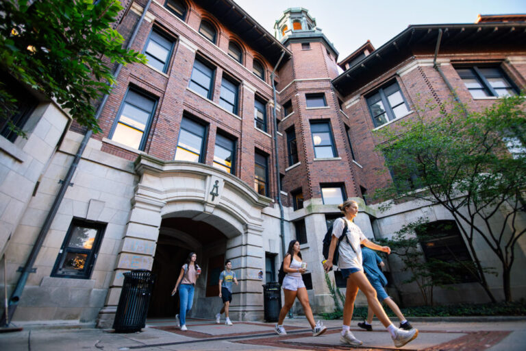 Students walk past a large brick building