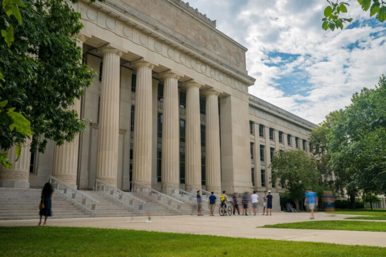 A large building with pillars and several people walking in front