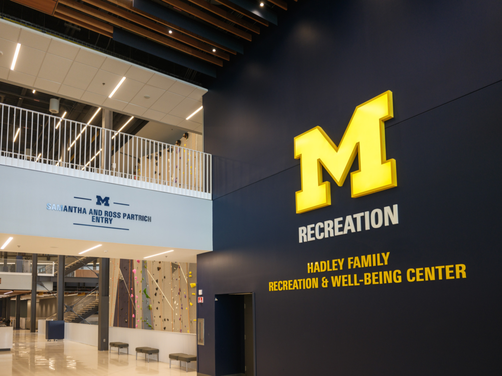 A bright maize block M with the words Recreation and Hadley Family Recreation & Well-Being Center against a blue wall