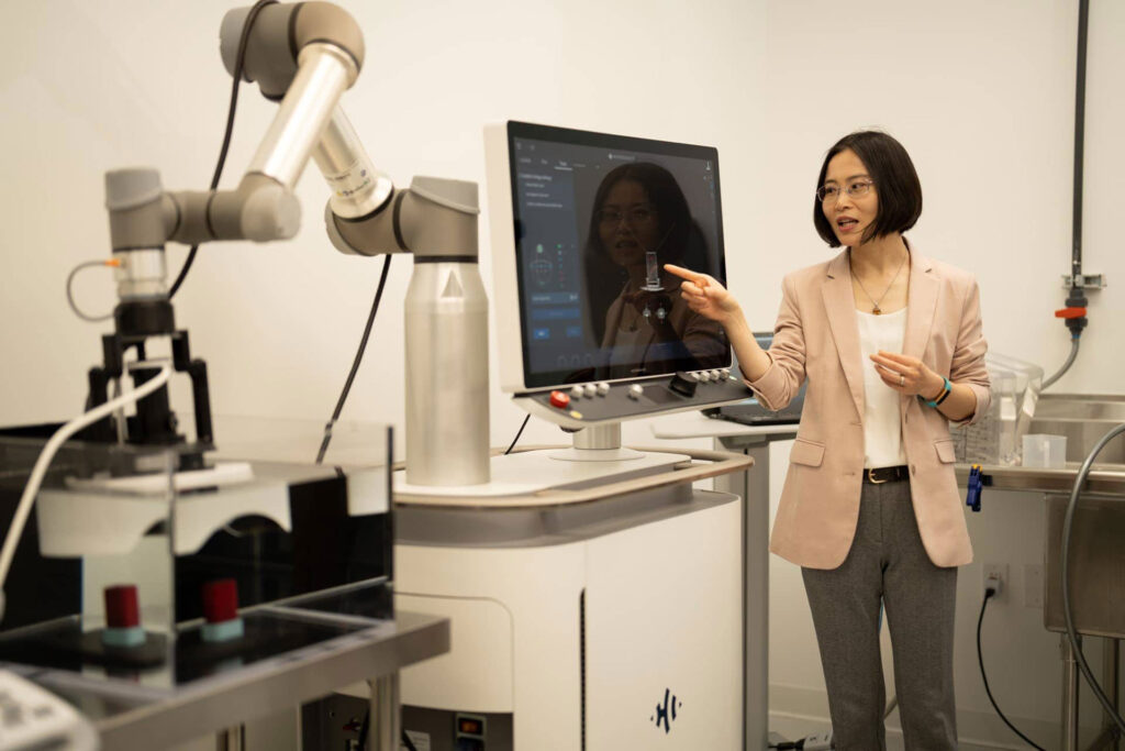 A woman stands and points at a computer screen while speaking